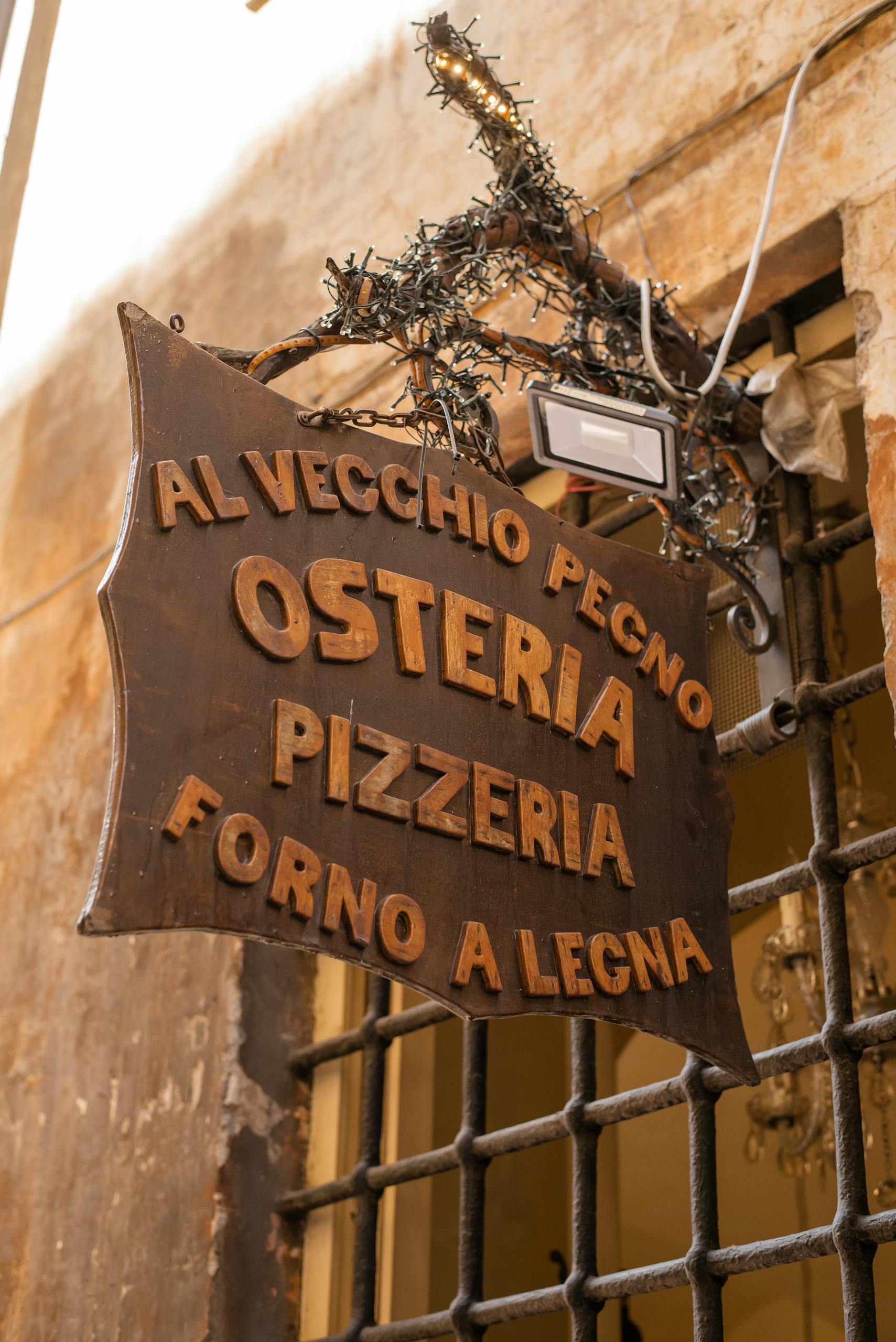 Charming wooden sign of Italian osteria and pizzeria on a sunny street.