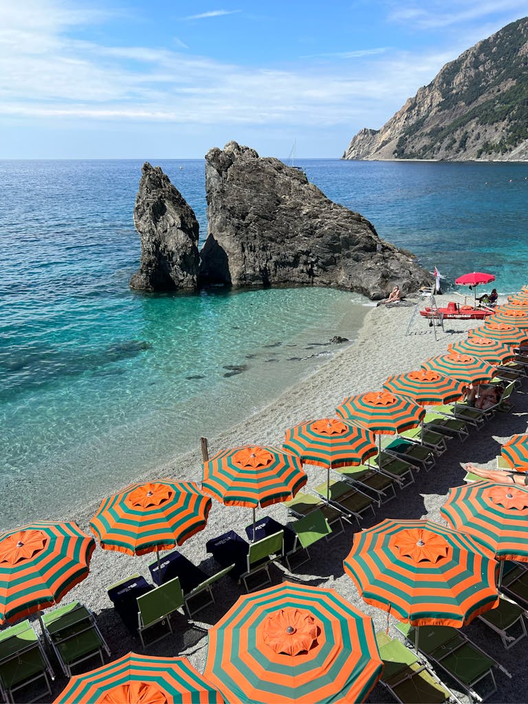 Colorful beach umbrellas on an Italian coast with rocky formations and turquoise sea.