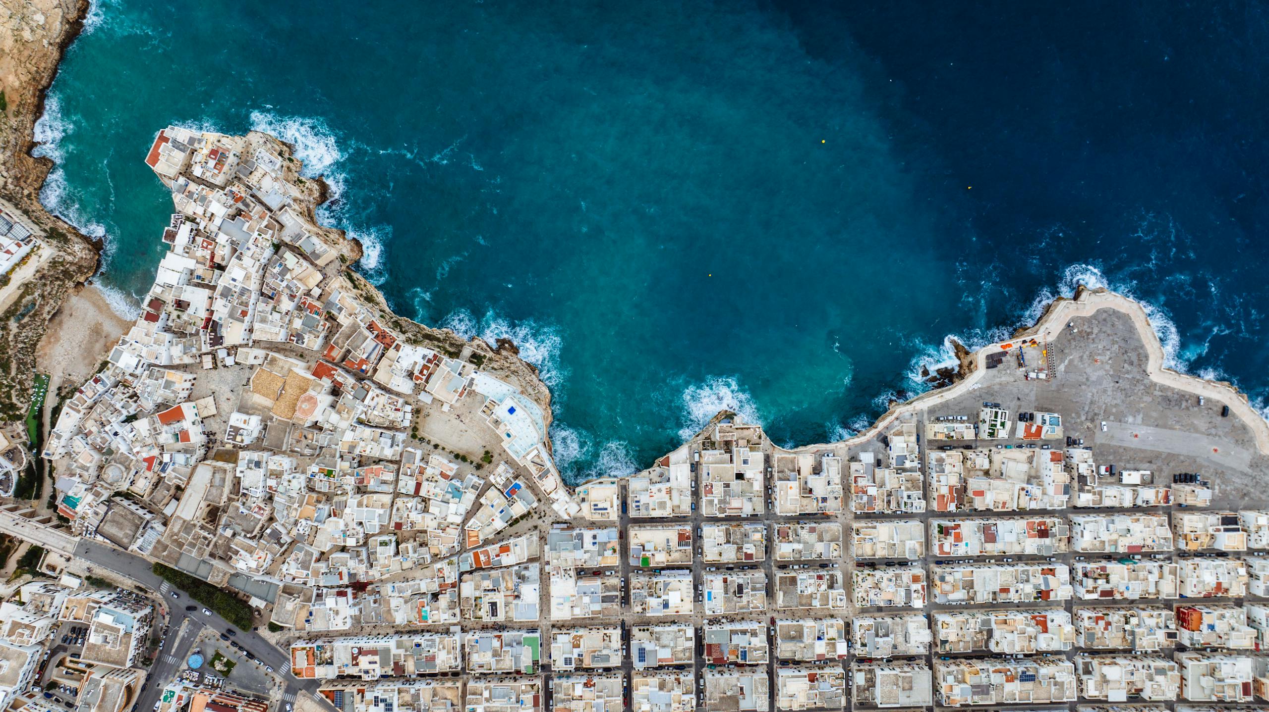 Drone shot of Polignano a Mare showcasing urban coastline against the blue sea.
