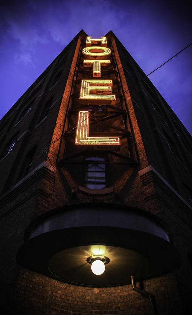 Eye-catching low angle shot of a neon hotel sign illuminating a brick building facade at dusk.