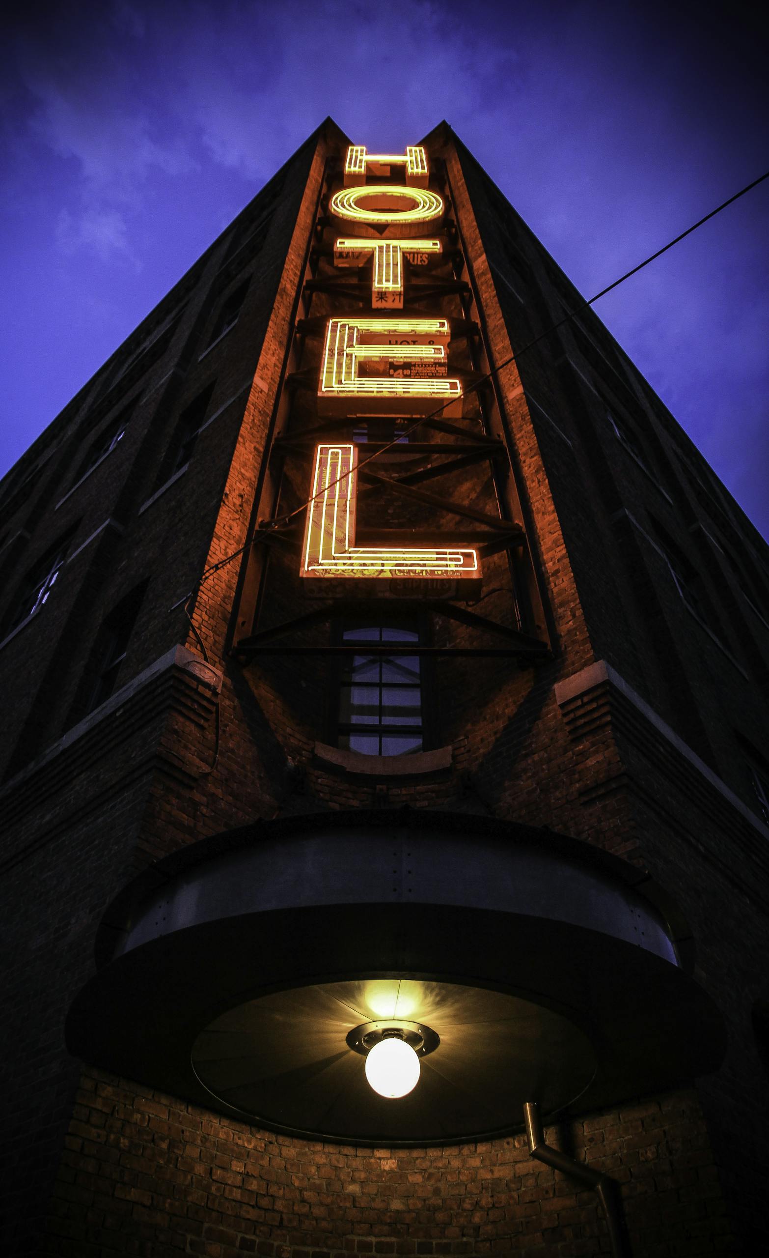 Eye-catching low angle shot of a neon hotel sign illuminating a brick building facade at dusk.