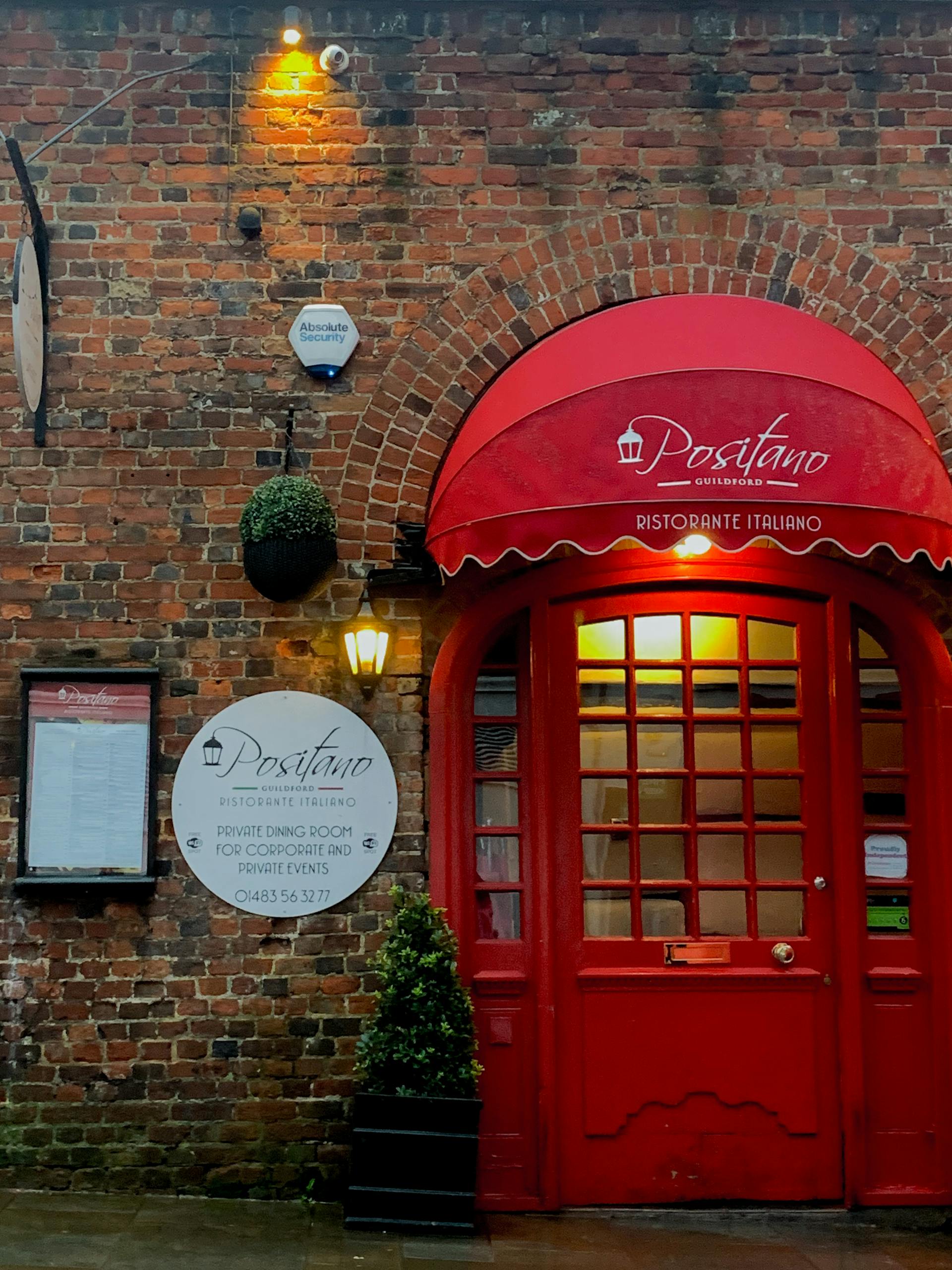 Red door entrance of an Italian restaurant with brick wall and signage, creating a cozy urban atmosphere.